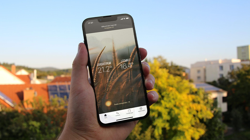 En hand håller en mobil med Ngenics app om värmestyrning.