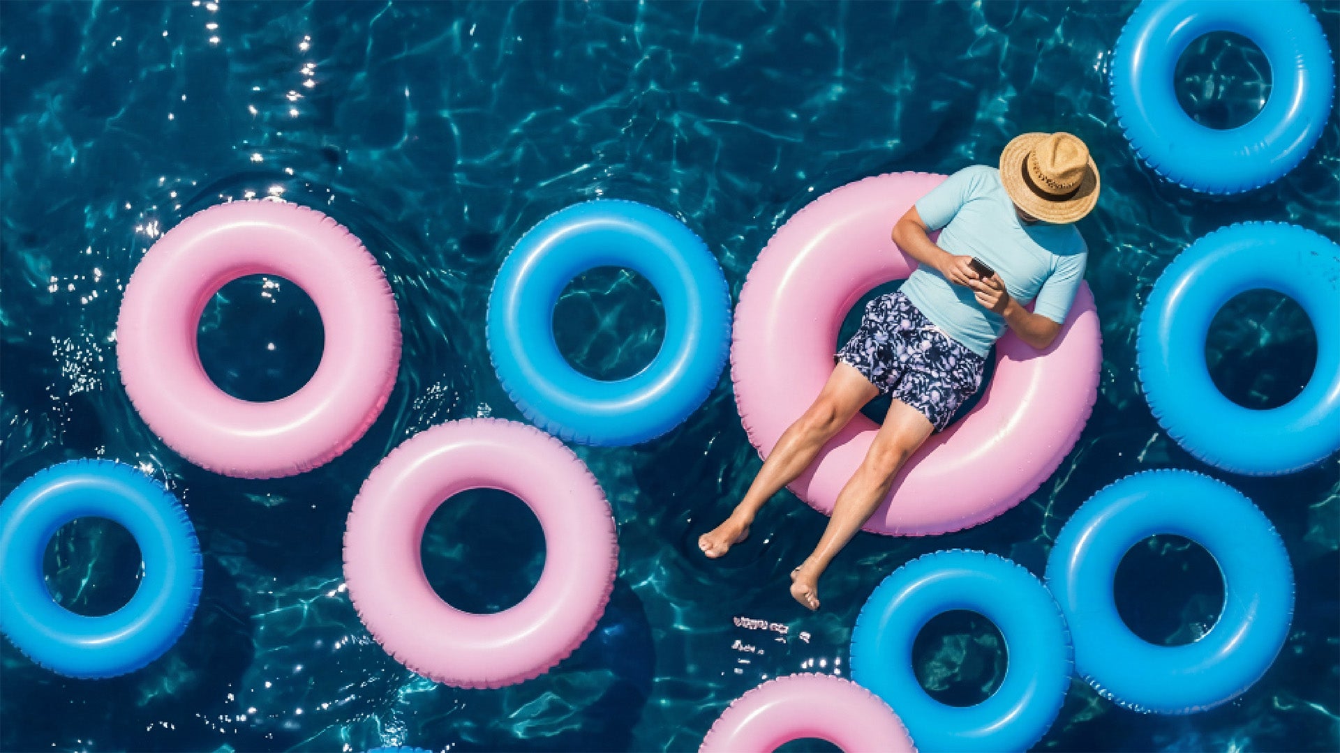 Man med solhatt badar i en rosa badring i en pool med många badringar i blått och rosa.