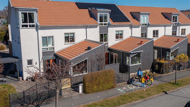 Radhuslänga med solpaneler på taket i ett bostadsområde i Jönköping, där barn ritar med gatukritor på gångbanan utanför.