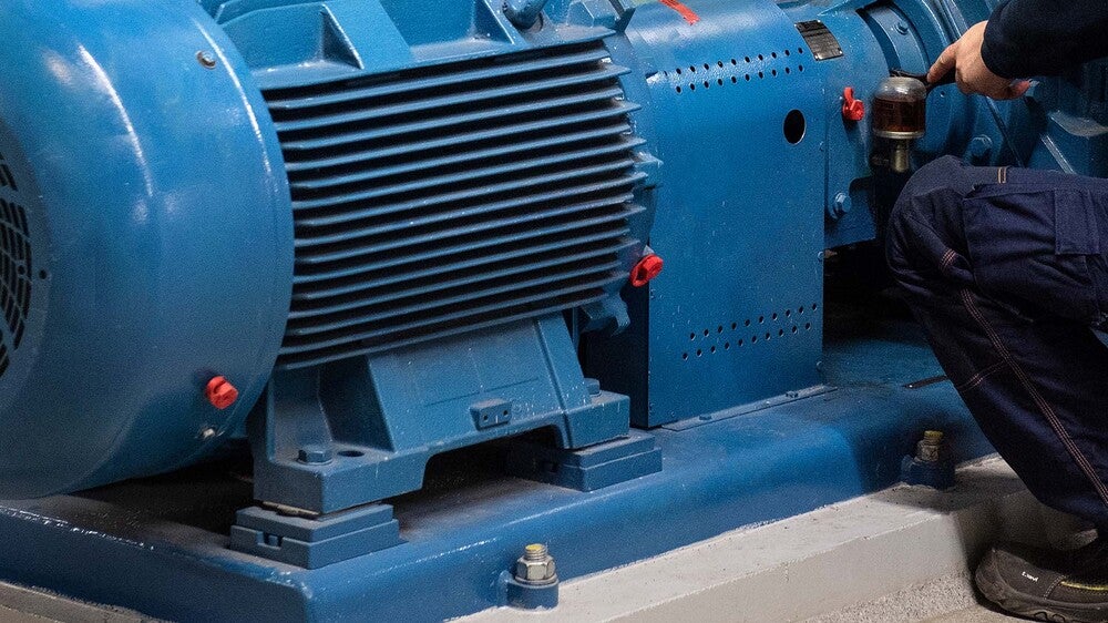 En tekniker utför underhåll på en stor blå industriell motor, med fokus på maskinens detaljer och dess robusta konstruktion.