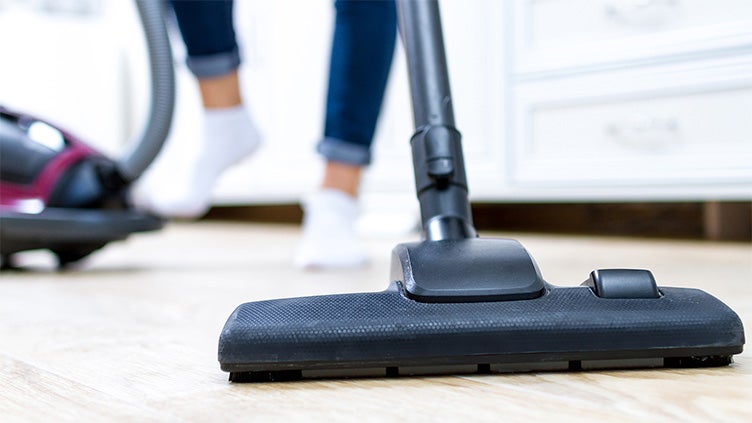 Närbild på dammsugare i användning på ett trägolv, med en person i bakgrunden i strumpor och jeans – illustrerar vardaglig elanvändning i hushållet.