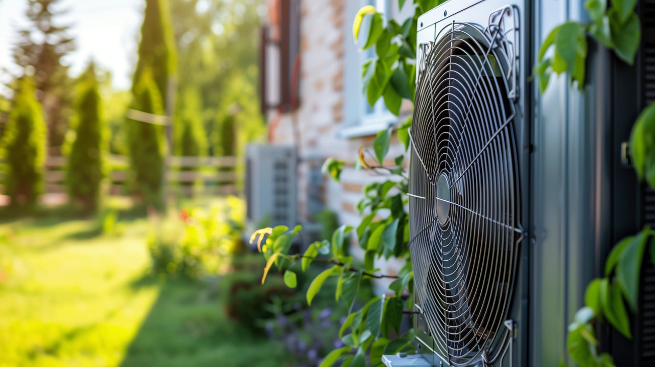 En fläkt till en vattenburen värmepump i en somrig trädgård.