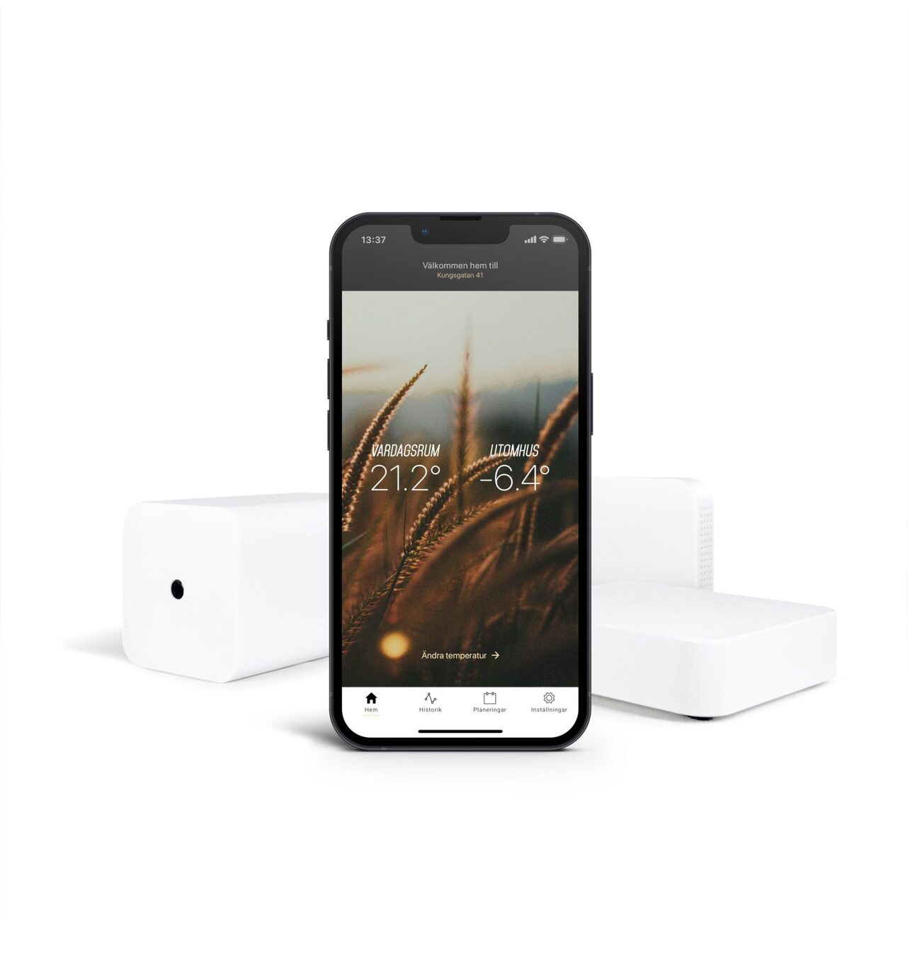 I förgrunden syns en mobil med Ngenics app. I bakgrunden syns produkter till värmestyrning.