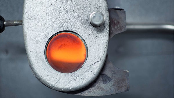 Närbild på ett runt inspektionsglas i metallram där den glödande elden syns inuti en förbränningsugn