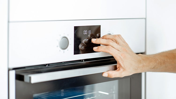 En hand vrider på kontrollen på en modern ugn med digital display. Ugnen har en minimalistisk design med en rostfri handtag och glasdörr.