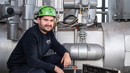 Fjärvärmetekniker med grön hjälm sitter framför stora rör.