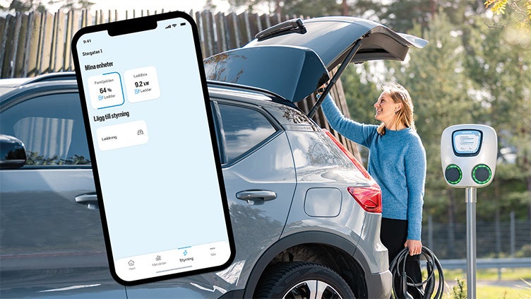 Kvinna vid en silverfärgad elbil kopplar in laddkabel vid laddstation, medan en mobilapp på skärmen visar information om laddningens status.