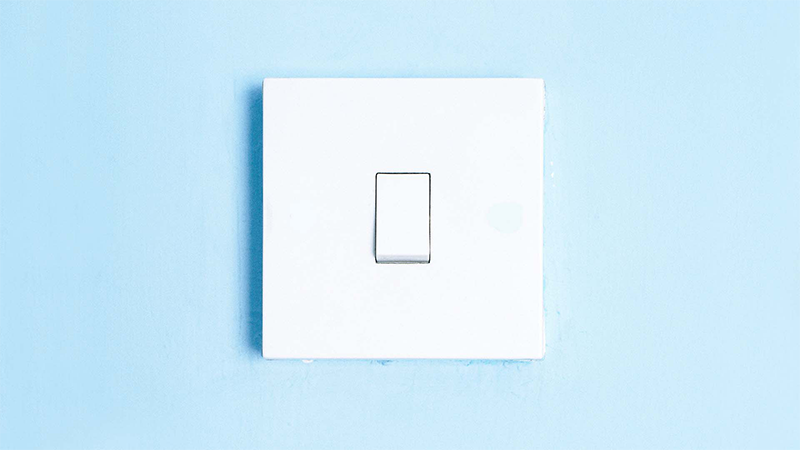 Vit strömbrytare monterad på en ljusblå vägg i närbild.