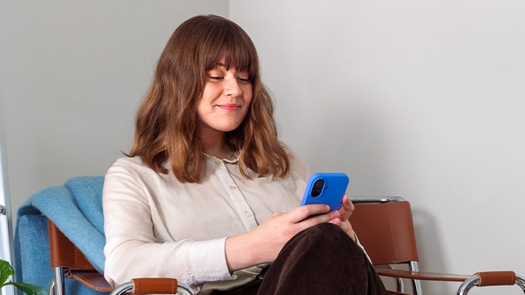 Kvinna sitter i fåtölj och tittar i en blå mobiltelefon.