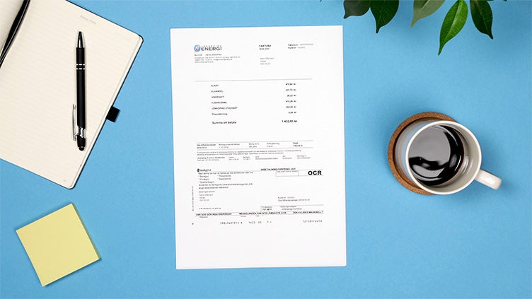 Faktura ligger på ett blått skrivbord bredvid anteckningsblock, penna, post-it-lappar, kaffekopp och växt.