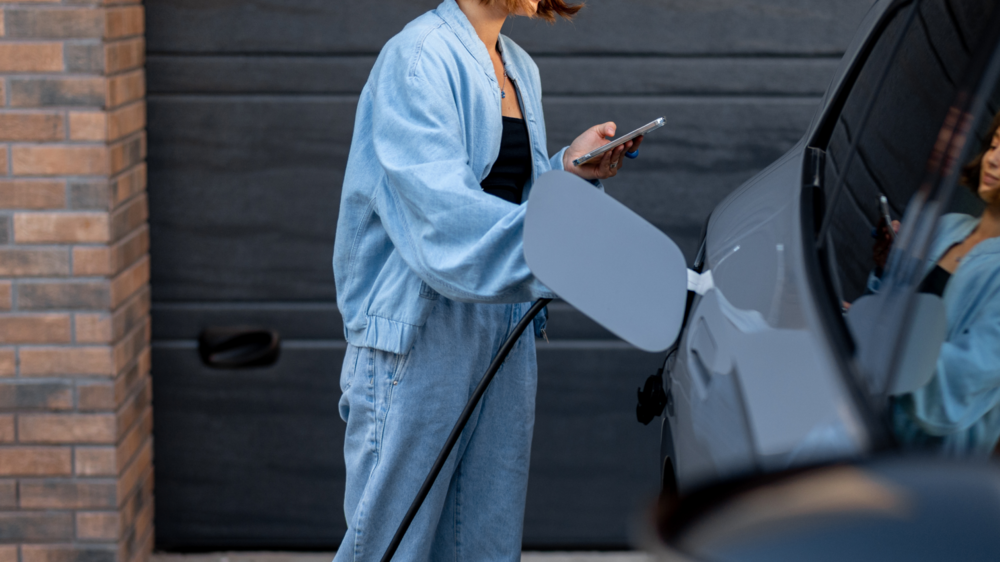 En person laddar bilen hemma, och tittar i mobilen.