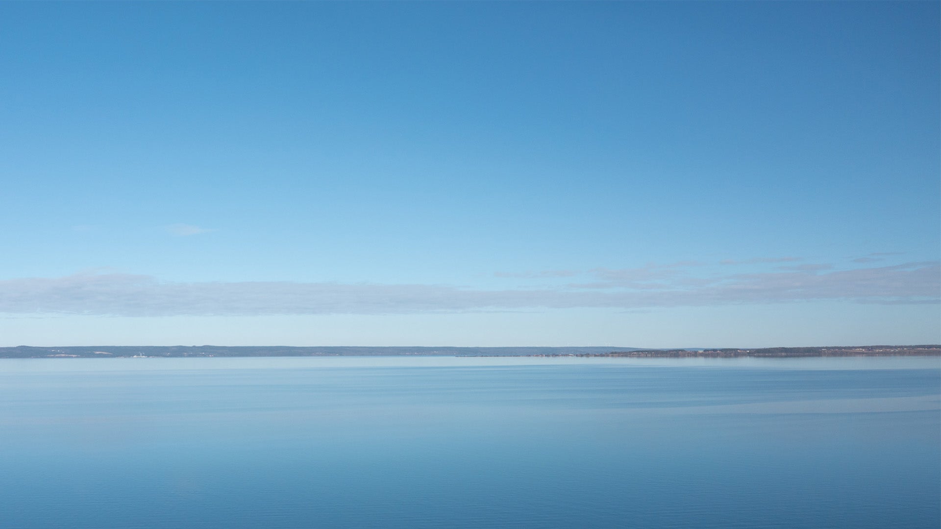 En vidsträckt vy över den lugna sjön Vättern, där himlen och vattnet smälter samman i blå nyanser. Horisonten är tydlig och sträcker sig över hela bilden, vilket skapar en känsla av ro och öppenhet.