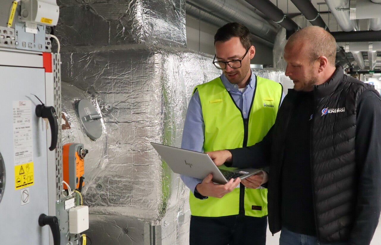 två medarbetare från jönköping energi står i en industriell miljö och diskuterar samtidigt som de kollar på en laptop.