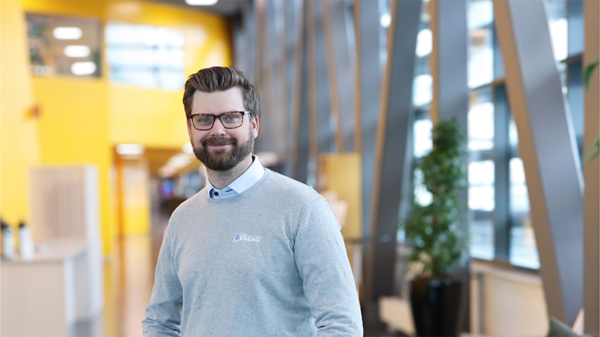 Leende man med glasögon och grå tröja med Jönköping Energi-logotyp står i ljus kontorsmiljö med gula väggar och stora fönster