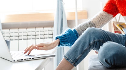 Hand sträcker sig mot en bärbar dator i hemmiljö med element i bakgrunden